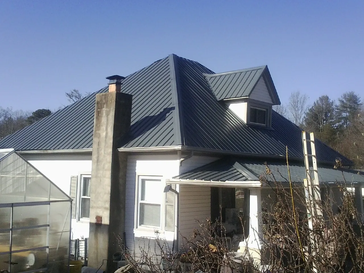 Dark blue standing seam metal roof on a white farmhouse with dormer — Slate & Tile Roof Repair by Roofing Brothers in Langlois