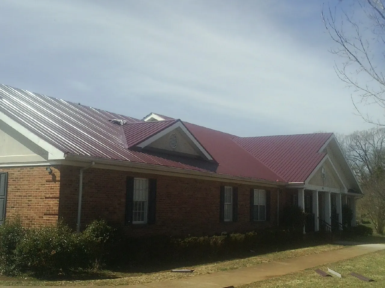 Red metal roof with gabled entries on a long brick building, from a Hail Damage Roof Repair job in Langlois