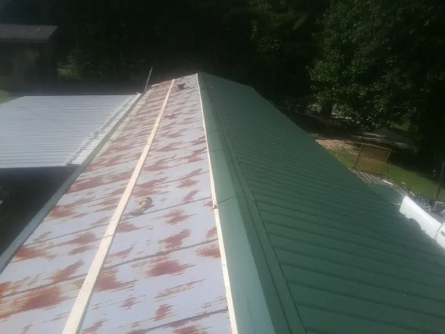 Old rusted panels beside newly installed green metal roofing — Wind Damage Roof Repair by Roofing Brothers in Langlois