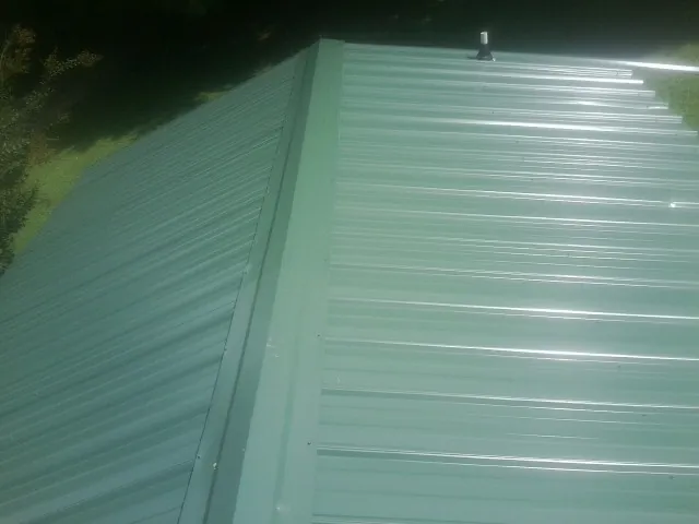 New green metal panels meeting at the ridge of a roof — Flat Roof Repair work by our crew in Langlois
