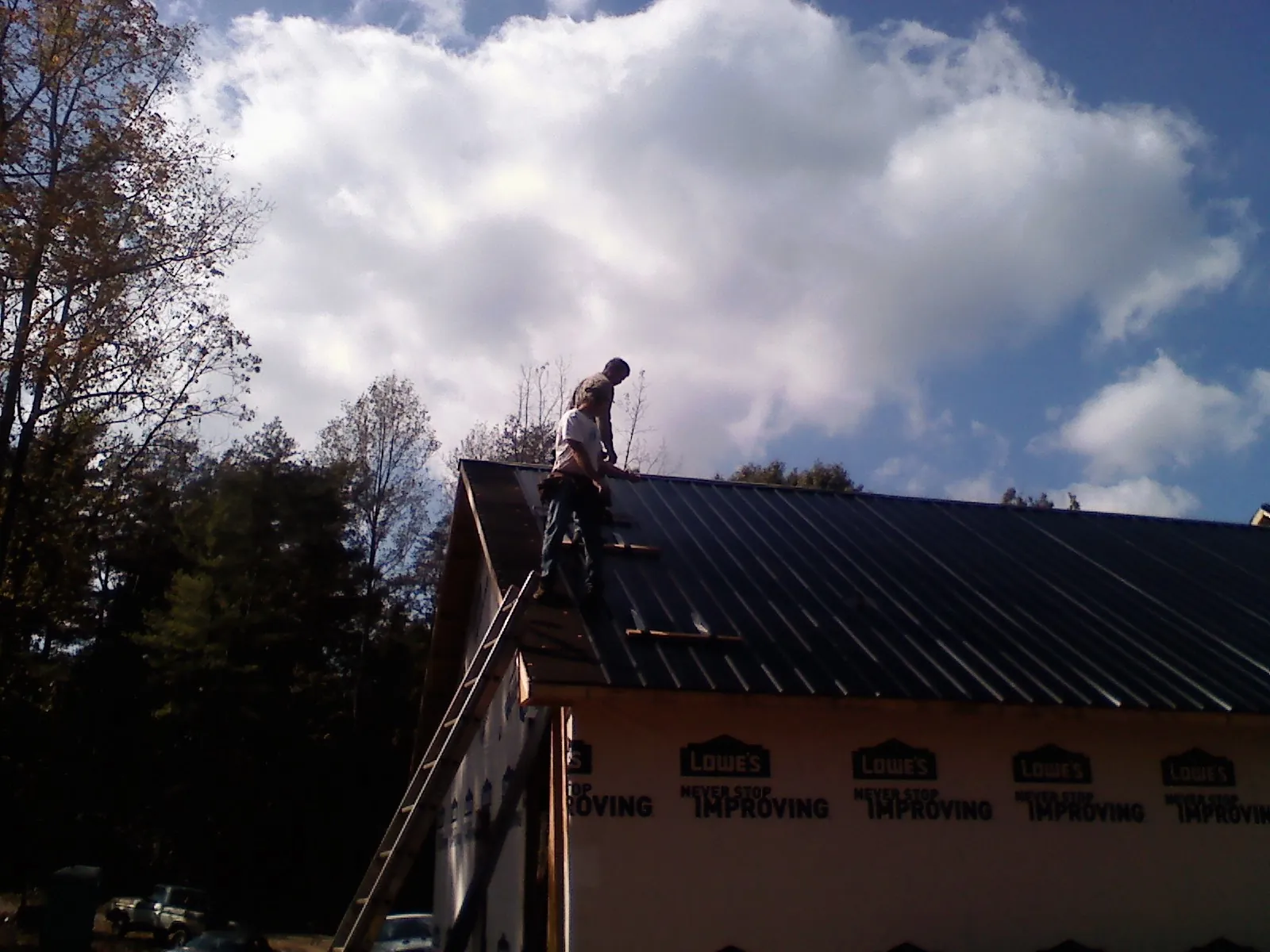 Roofer fastening dark metal panels high against a cloudy sky, from a Roof Inspection job in Langlois