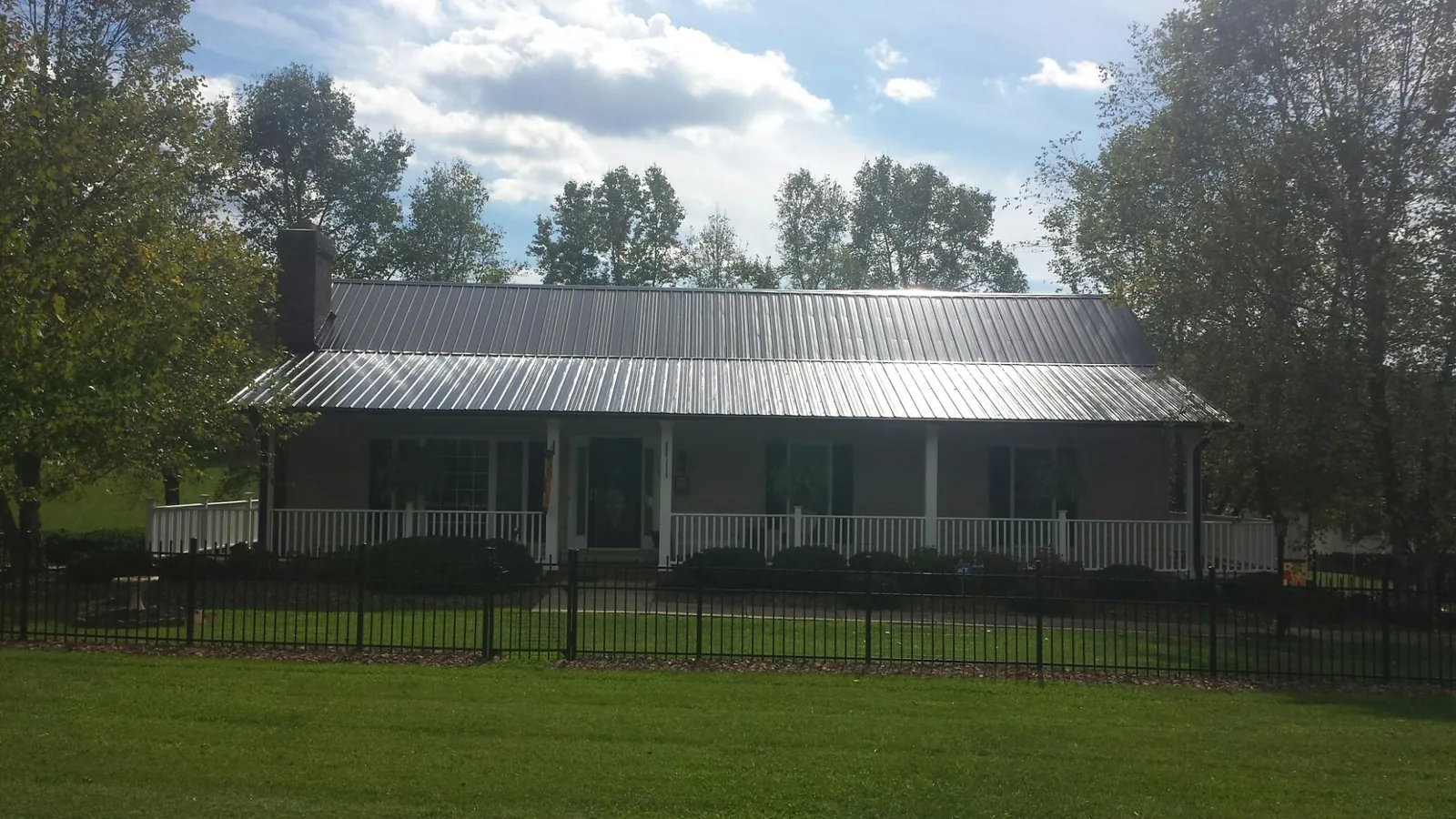 Gray metal roof on a brick ranch with a full width front porch — Gutter Guard Installation work by our crew in Langlois