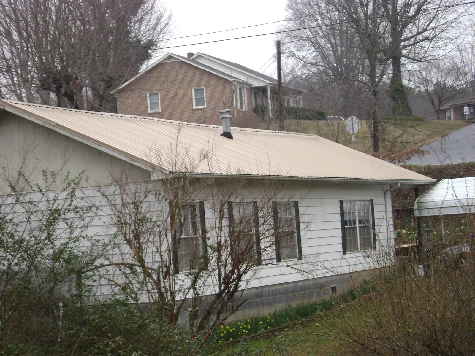 Tan metal roof on a white sided house set into a hillside — Commercial Roofing by Roofing Brothers in Langlois