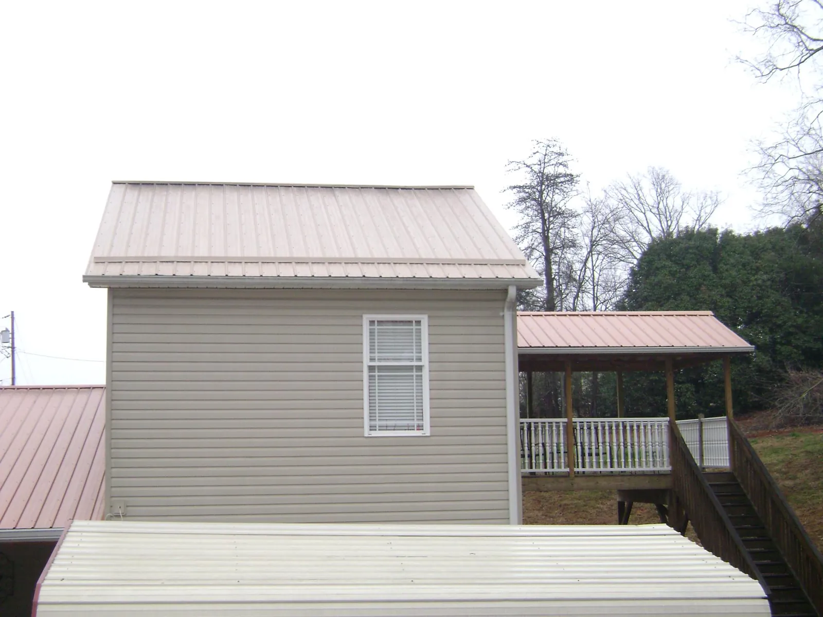 Tan metal roofs on a two story addition and attached porch, from a Roof Replacement job in Langlois